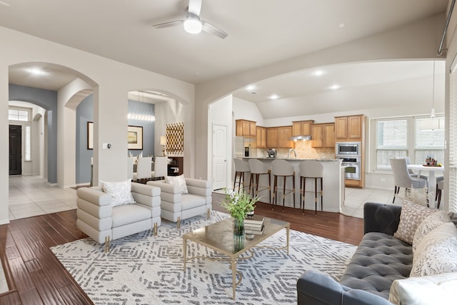 living area with arched walkways, lofted ceiling, ceiling fan, light wood-type flooring, and recessed lighting