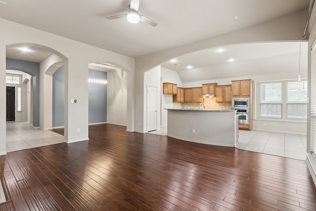 unfurnished living room featuring arched walkways, a ceiling fan, baseboards, vaulted ceiling, and light wood-type flooring