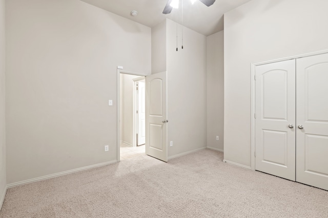 unfurnished bedroom featuring a closet, a towering ceiling, light carpet, ceiling fan, and baseboards