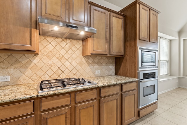 kitchen featuring light stone counters, light tile patterned flooring, under cabinet range hood, stainless steel appliances, and backsplash