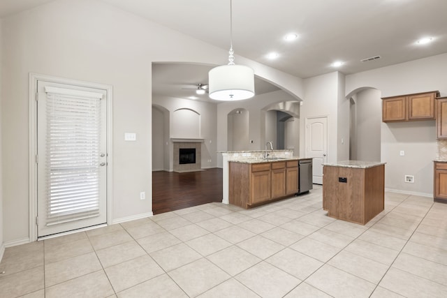 kitchen with brown cabinets, decorative light fixtures, a center island with sink, and visible vents