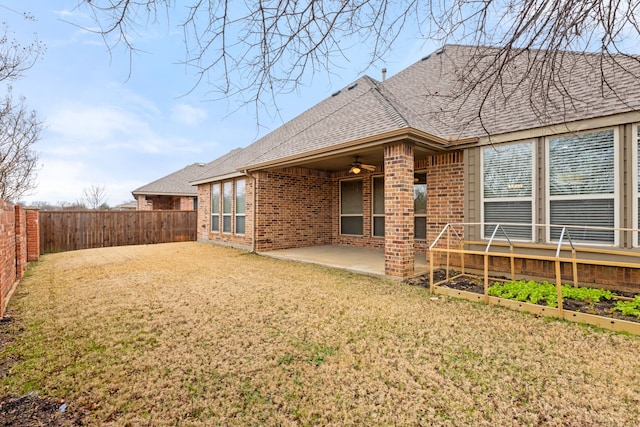 rear view of property featuring brick siding, roof with shingles, a lawn, a patio area, and a fenced backyard