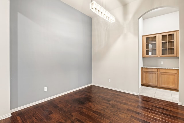 unfurnished dining area with arched walkways, light wood finished floors, and baseboards