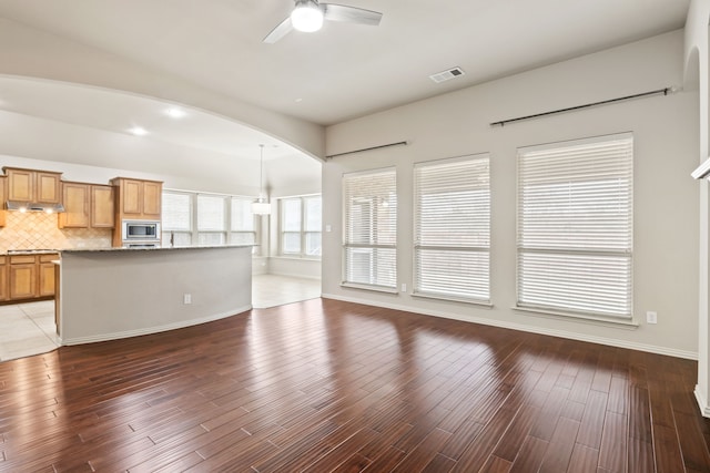 unfurnished living room featuring ceiling fan, dark wood-style flooring, arched walkways, and baseboards