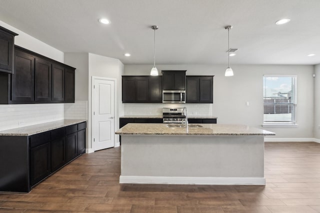 kitchen with a center island with sink, appliances with stainless steel finishes, dark hardwood / wood-style floors, and decorative light fixtures