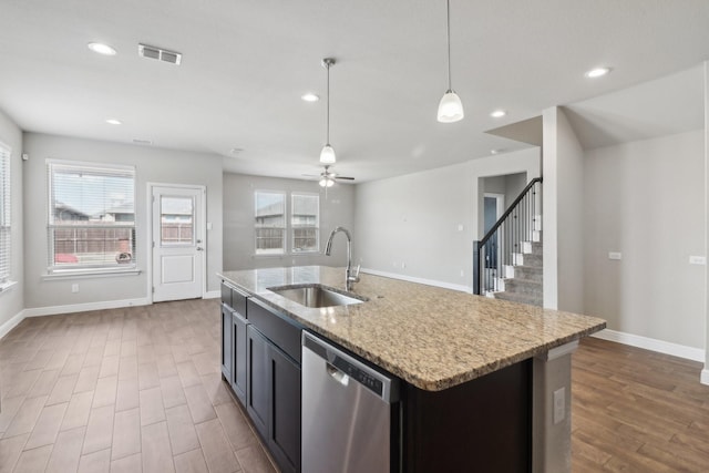 kitchen featuring a center island with sink, hanging light fixtures, light stone countertops, sink, and dishwasher