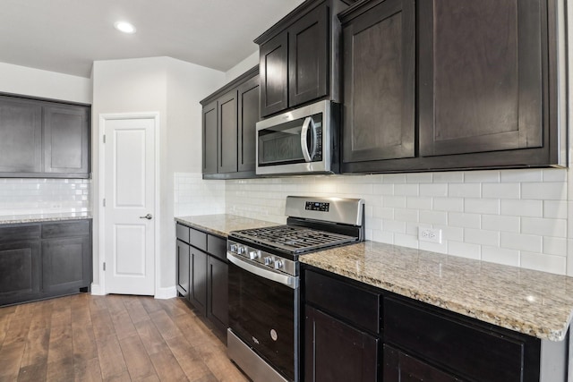 kitchen with dark brown cabinetry, stainless steel appliances, light stone countertops, backsplash, and dark hardwood / wood-style flooring