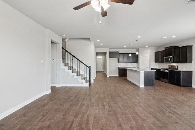 kitchen featuring an island with sink, backsplash, wood-type flooring, appliances with stainless steel finishes, and pendant lighting