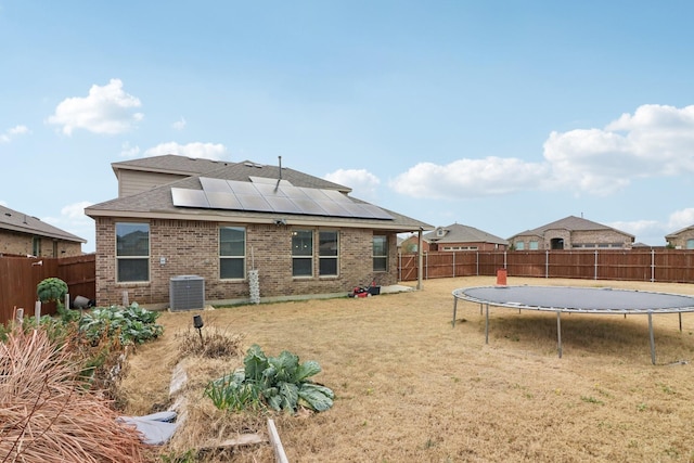 back of house featuring a trampoline, solar panels, a yard, and central AC