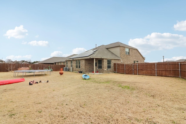 rear view of house with a trampoline, solar panels, central AC unit, and a lawn