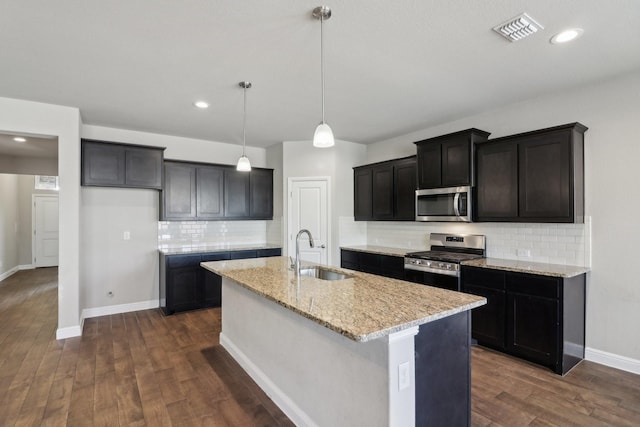 kitchen featuring a center island with sink, stainless steel appliances, light stone countertops, decorative light fixtures, and sink