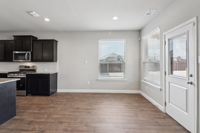 kitchen with hardwood / wood-style floors, appliances with stainless steel finishes, backsplash, and light stone counters