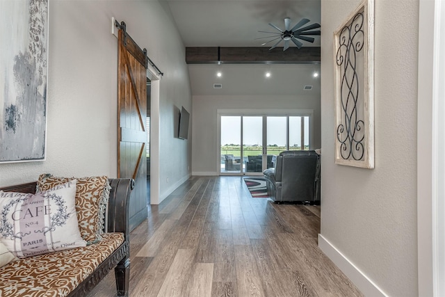 hall with visible vents, baseboards, a barn door, beamed ceiling, and light wood-type flooring