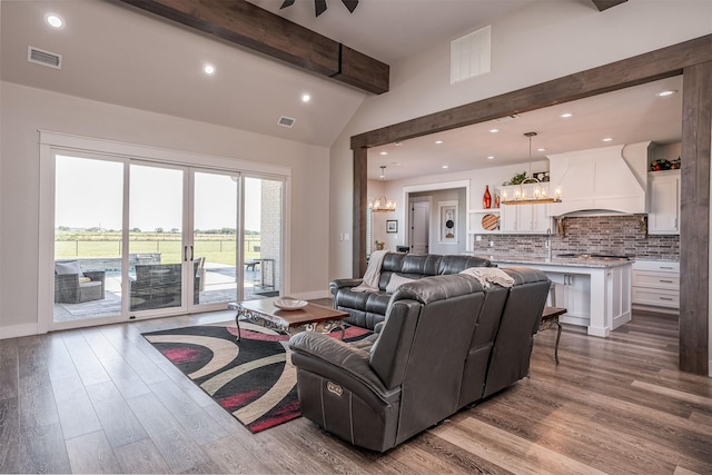 living area with light wood-type flooring, visible vents, an inviting chandelier, and beam ceiling