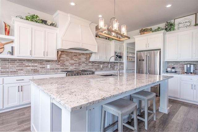 kitchen with custom exhaust hood, a kitchen island with sink, white cabinetry, and a sink