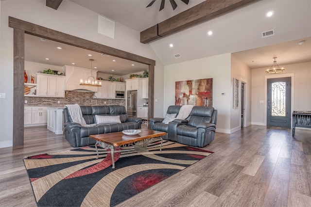 living area featuring a notable chandelier, visible vents, vaulted ceiling with beams, and light wood-style floors