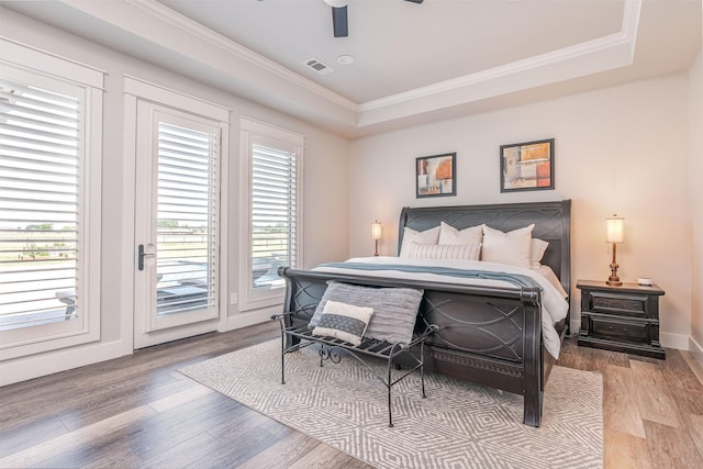 bedroom with light wood-style floors, a raised ceiling, visible vents, and access to outside