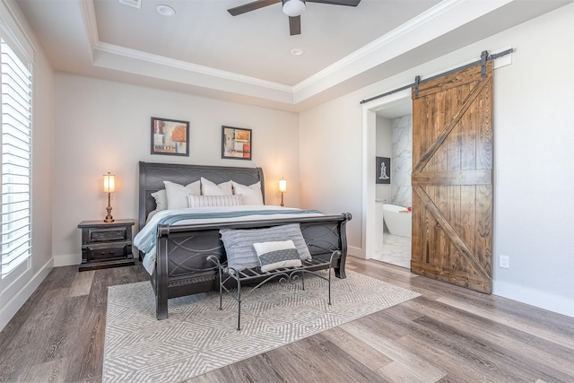 bedroom featuring crown molding, a barn door, a raised ceiling, and wood finished floors