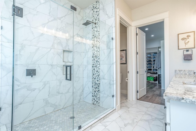 full bath featuring a spacious closet, vanity, marble finish floor, and a shower stall