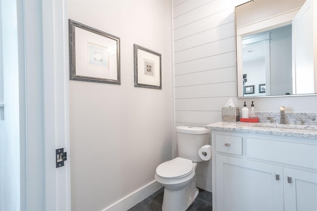 half bathroom with toilet, baseboards, vanity, and tile patterned flooring