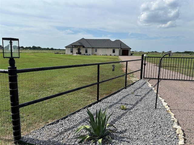 view of gate with a yard, fence, and a rural view