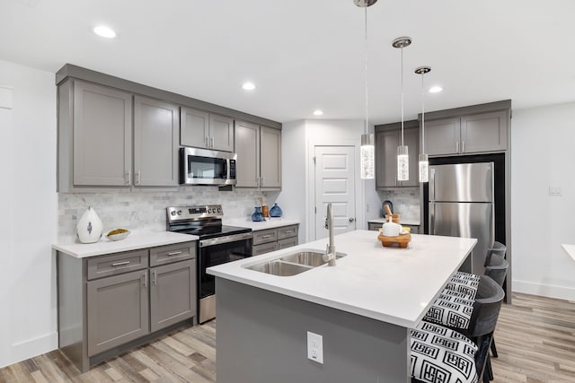 kitchen with light wood-type flooring, a center island with sink, decorative light fixtures, sink, and appliances with stainless steel finishes