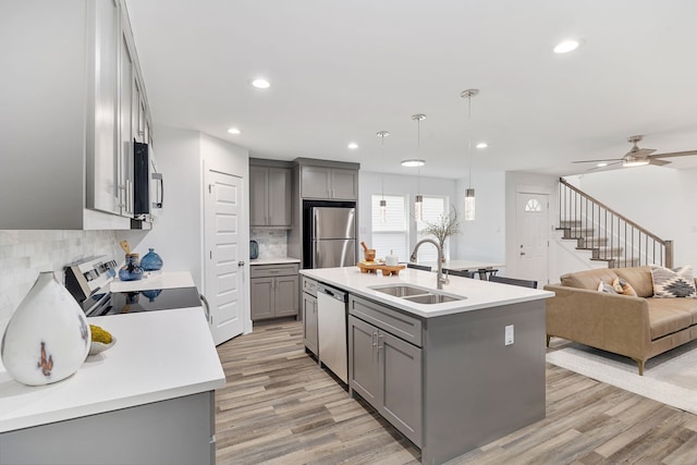 kitchen with sink, a kitchen island with sink, stainless steel appliances, and decorative light fixtures