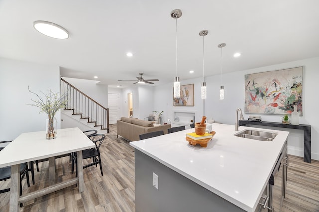 kitchen with sink, a center island with sink, light hardwood / wood-style floors, and pendant lighting