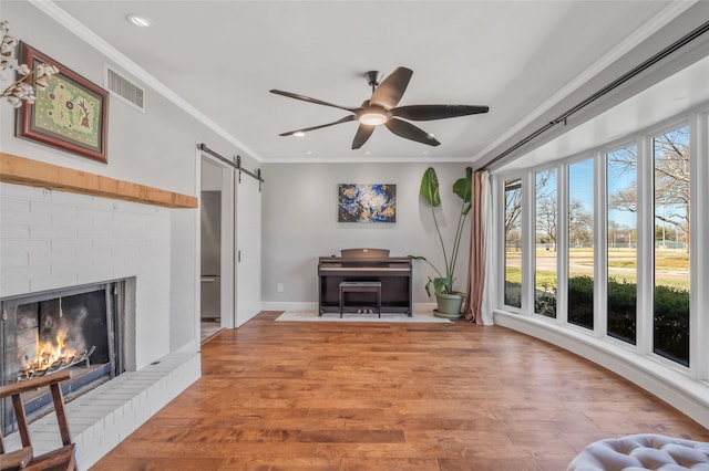 living area featuring a healthy amount of sunlight, a barn door, ornamental molding, and light wood-style flooring