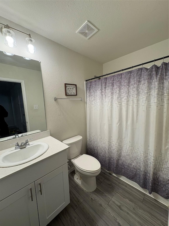 full bath with vanity, wood finished floors, visible vents, a textured ceiling, and toilet