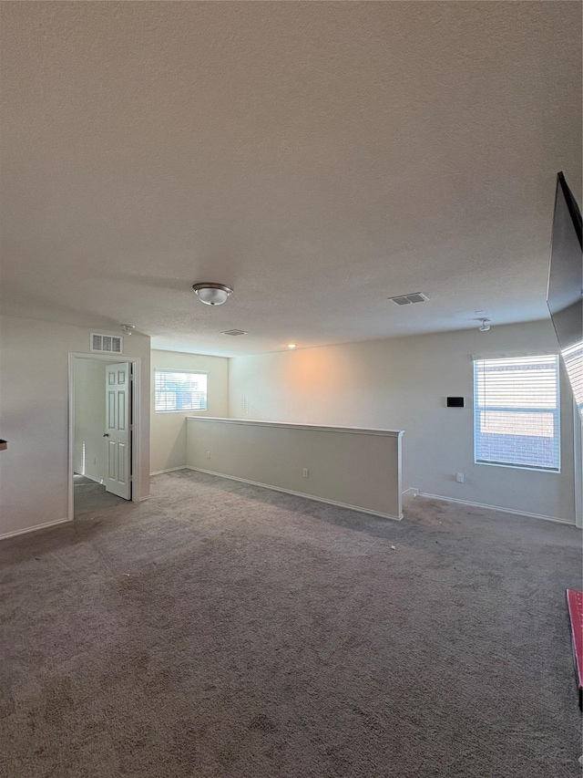 basement featuring visible vents, a textured ceiling, and carpet floors