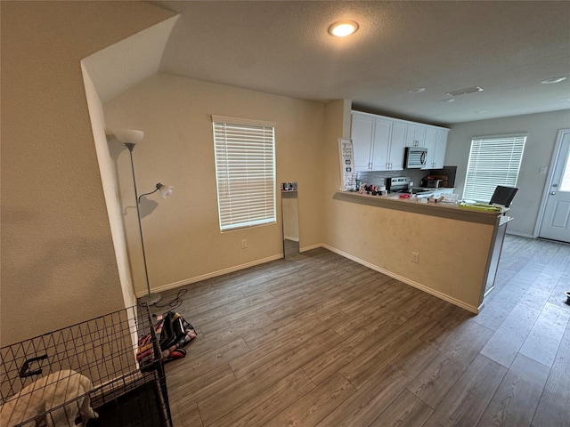 kitchen with kitchen peninsula, stainless steel appliances, wood-type flooring, white cabinets, and decorative backsplash