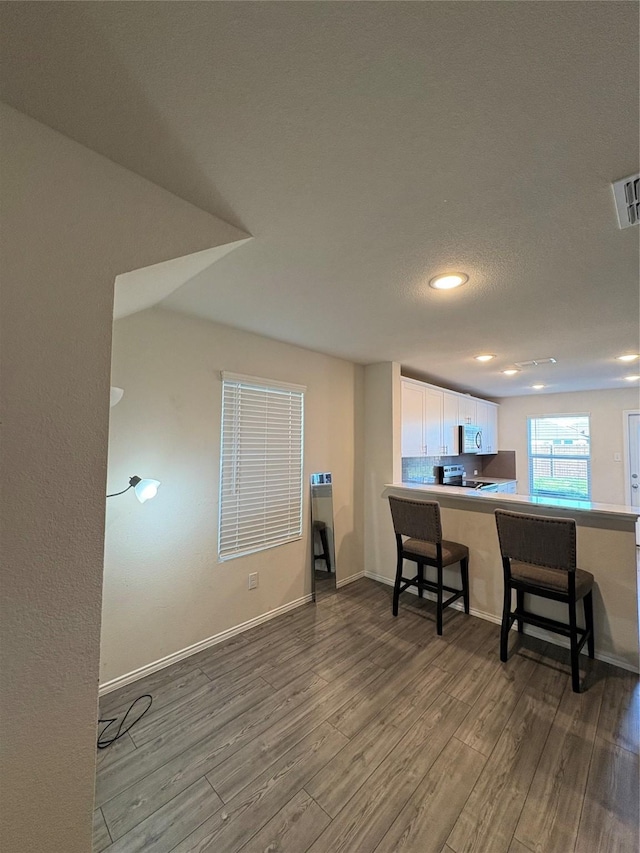 interior space featuring visible vents, wood finished floors, white cabinetry, a peninsula, and a breakfast bar area