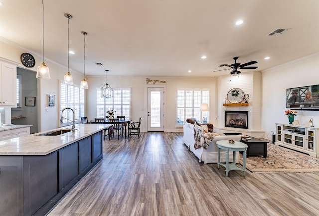 living room featuring sink, a large fireplace, ceiling fan, hardwood / wood-style floors, and crown molding