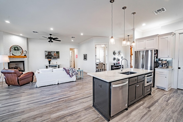 kitchen with an island with sink, decorative light fixtures, sink, appliances with stainless steel finishes, and white cabinets