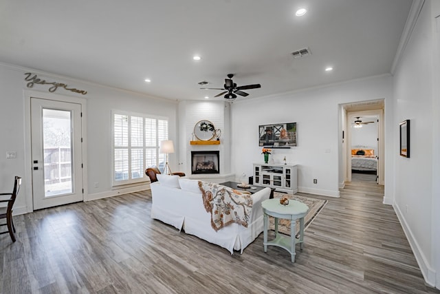 living room featuring a large fireplace, crown molding, ceiling fan, and wood-type flooring