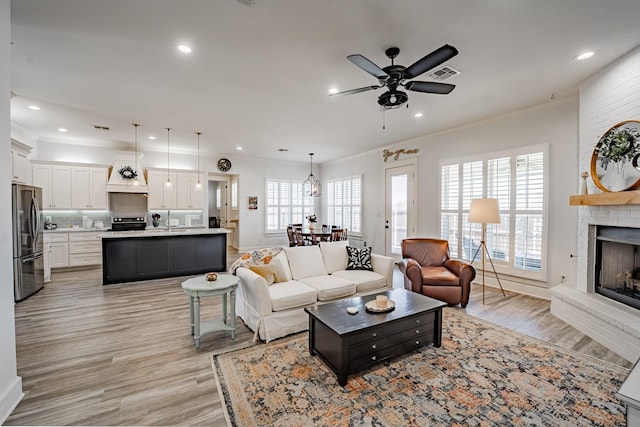 living room featuring ceiling fan, light hardwood / wood-style flooring, crown molding, and a fireplace