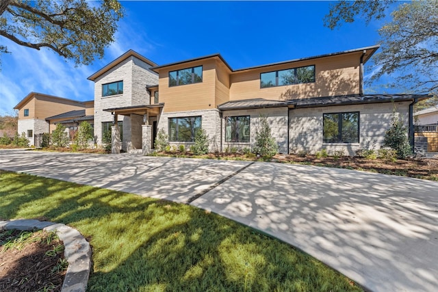 contemporary house with stone siding, a front yard, a standing seam roof, and metal roof