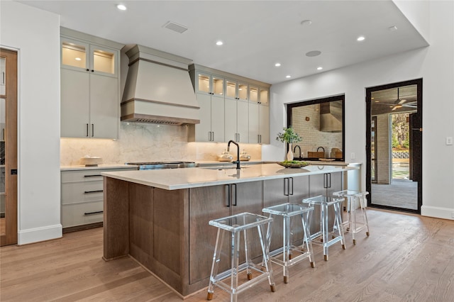 kitchen with a sink, light wood-type flooring, custom exhaust hood, and visible vents