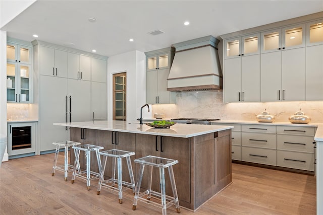 kitchen with visible vents, an island with sink, a kitchen breakfast bar, custom exhaust hood, and light wood-type flooring