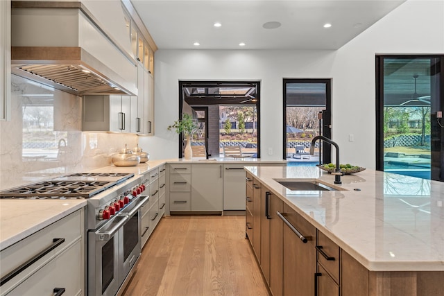 kitchen with light stone counters, custom range hood, light wood-style floors, a sink, and double oven range