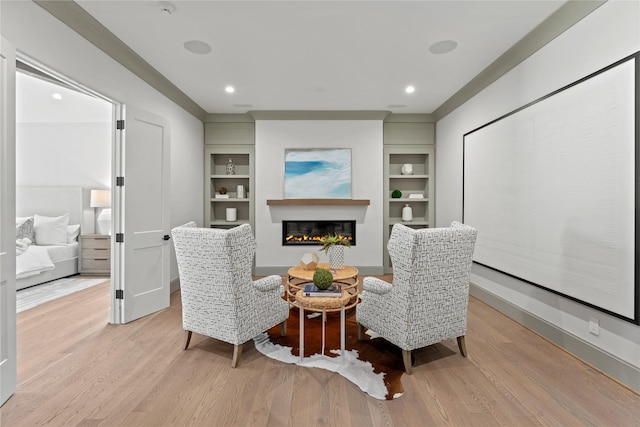 living area featuring recessed lighting, light wood-style flooring, built in shelves, and a glass covered fireplace