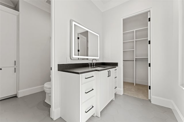 bathroom featuring a walk in closet, baseboards, vanity, and toilet