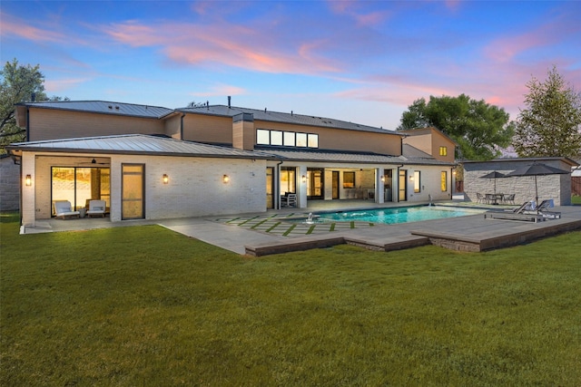 back of property at dusk with metal roof, brick siding, a lawn, a standing seam roof, and a patio area