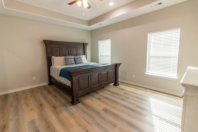 bedroom with ceiling fan, light hardwood / wood-style flooring, and a raised ceiling