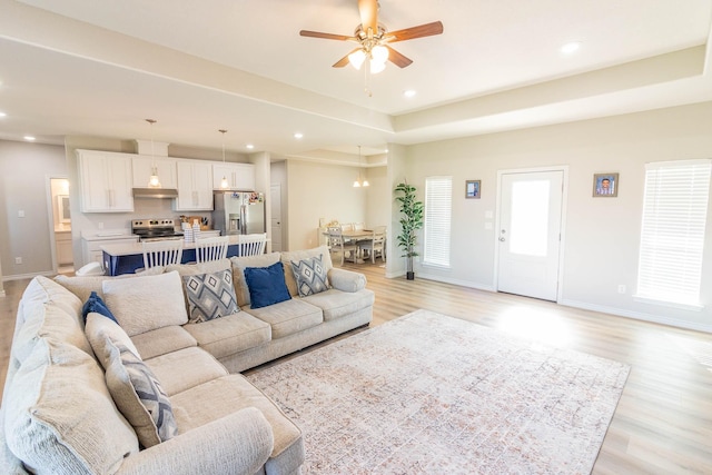 living room featuring a raised ceiling, ceiling fan, and light hardwood / wood-style flooring