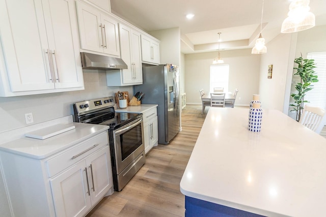 kitchen featuring appliances with stainless steel finishes, white cabinetry, light hardwood / wood-style floors, hanging light fixtures, and a raised ceiling