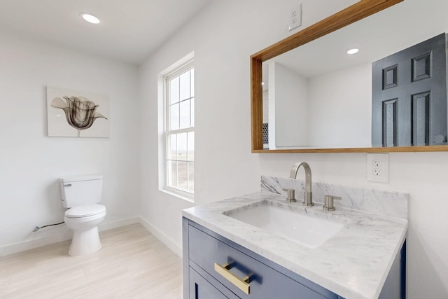 bathroom featuring vanity, wood finished floors, toilet, baseboards, and recessed lighting