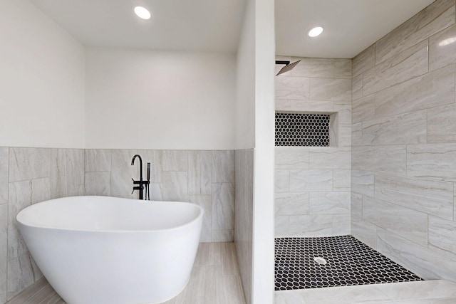 bathroom with a freestanding bath, tile walls, wainscoting, and tiled shower