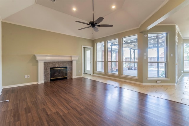 unfurnished living room featuring hardwood / wood-style flooring, vaulted ceiling, crown molding, and a tiled fireplace